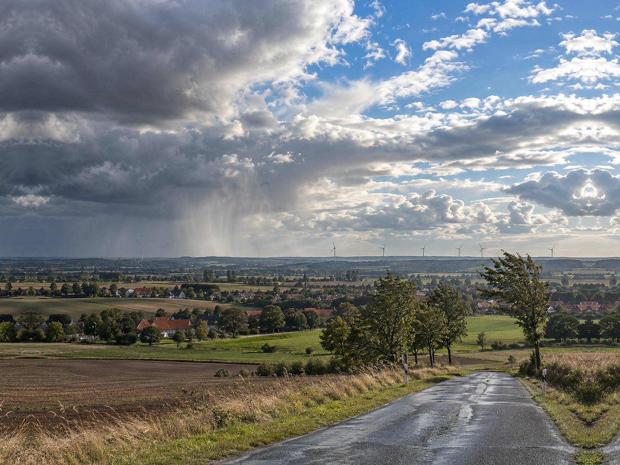 Wechselhaftes Herbstwetter über einer deutschen Landschaft mit nasser Straße, Schauern und Aufhellungen