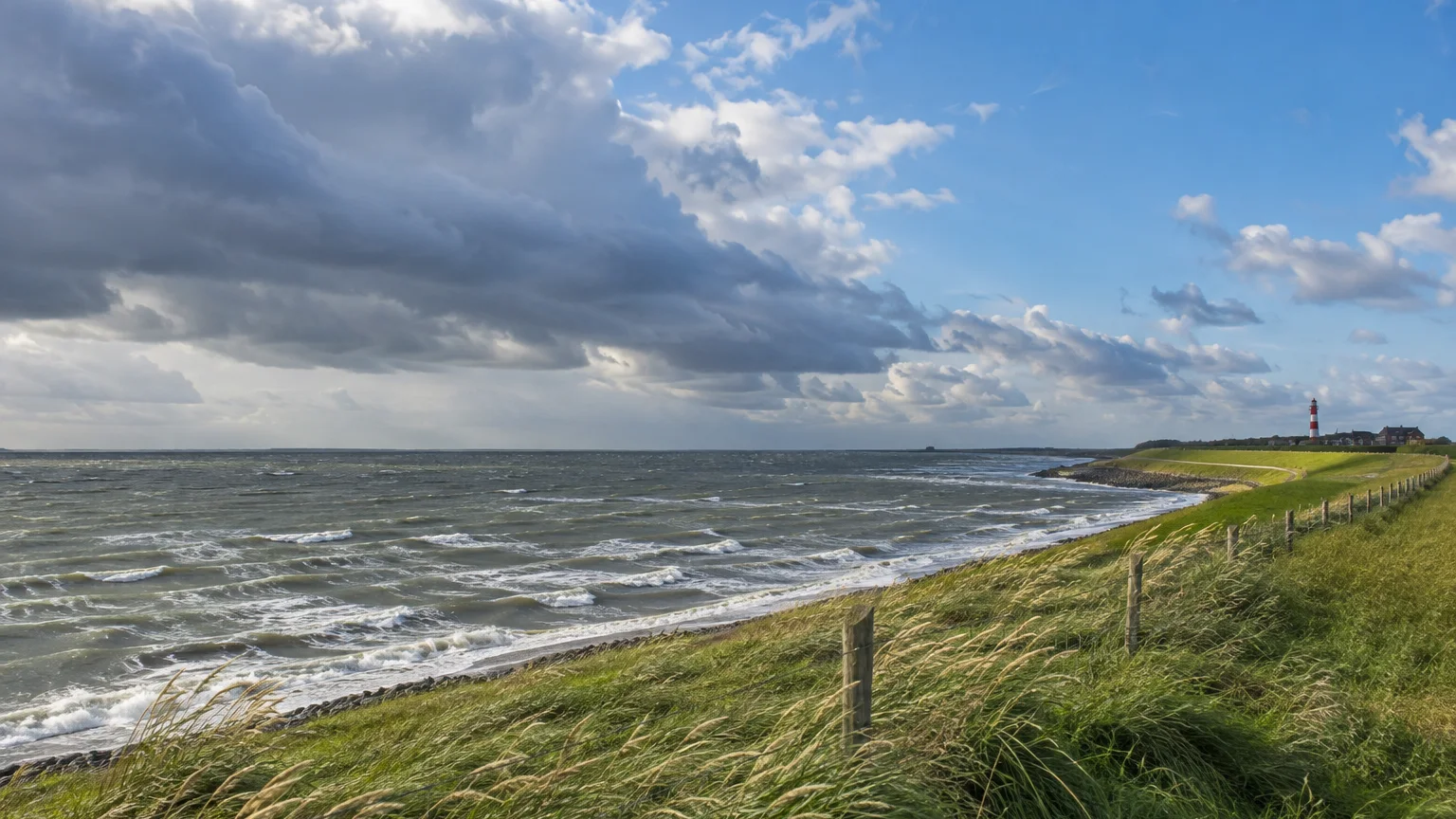 Windige Nordseeküste mit Deich, bewegter See und aufziehenden Wolken.