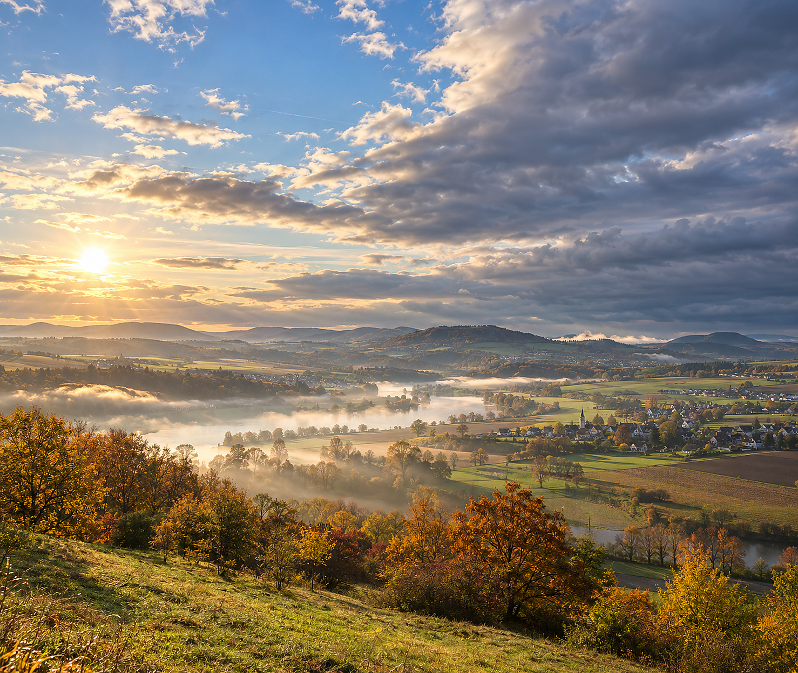 Herbstliches deutsches Flusstal mit Nebelfeldern, Sonne und dichter werdenden Wolken als Symbolbild für den Wetterwechsel am Mittwoch.