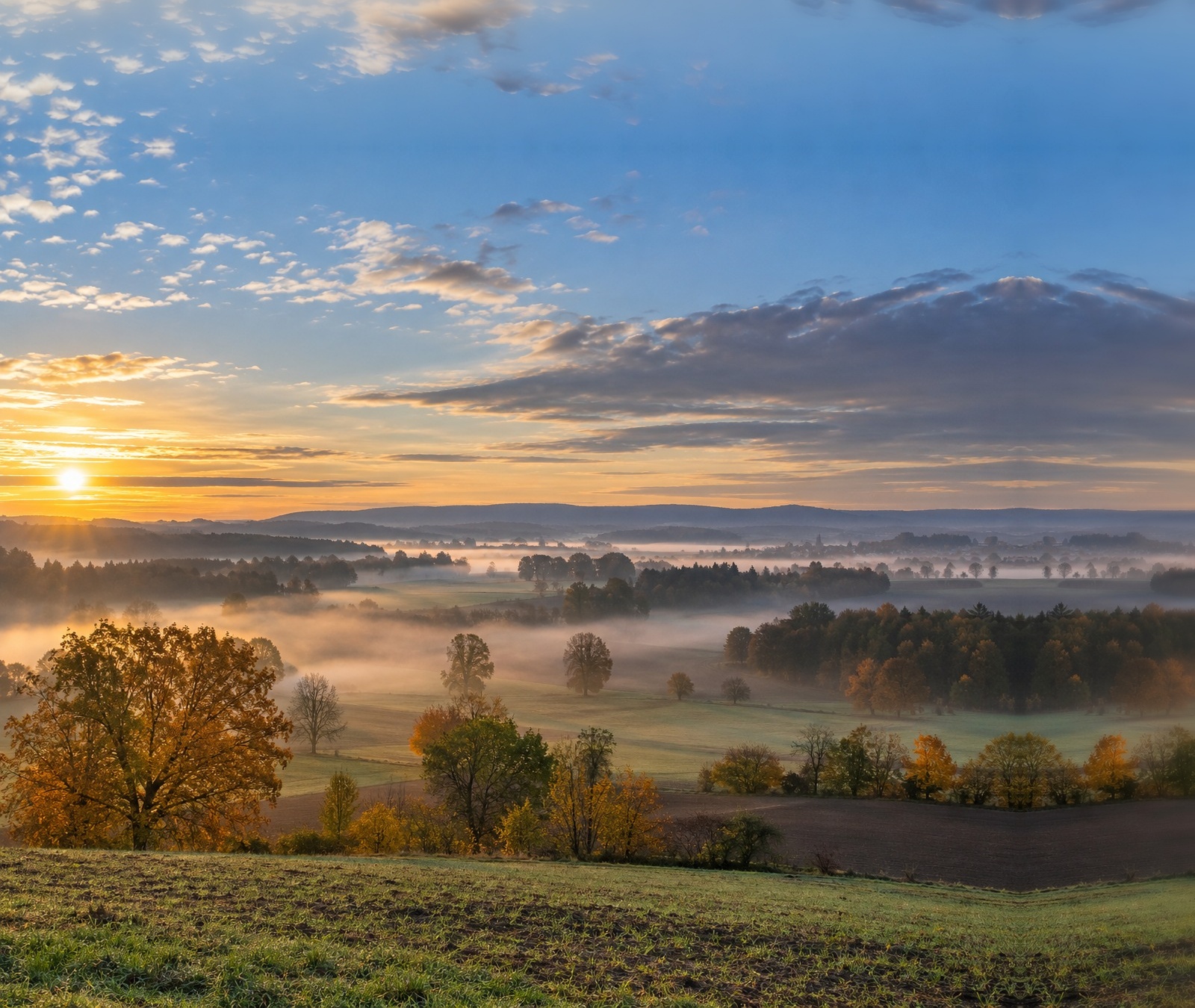 Goldener Herbstmorgen über einer deutschen Fluss- und Hügellandschaft mit Nebelfeldern als Symbolbild für freundliches Wetter nach Nebelauflösung.
